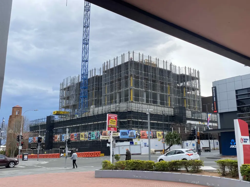 A multi-storey building under construction with scaffolding and a blue crane at the corner of Crown and Kembla Streets